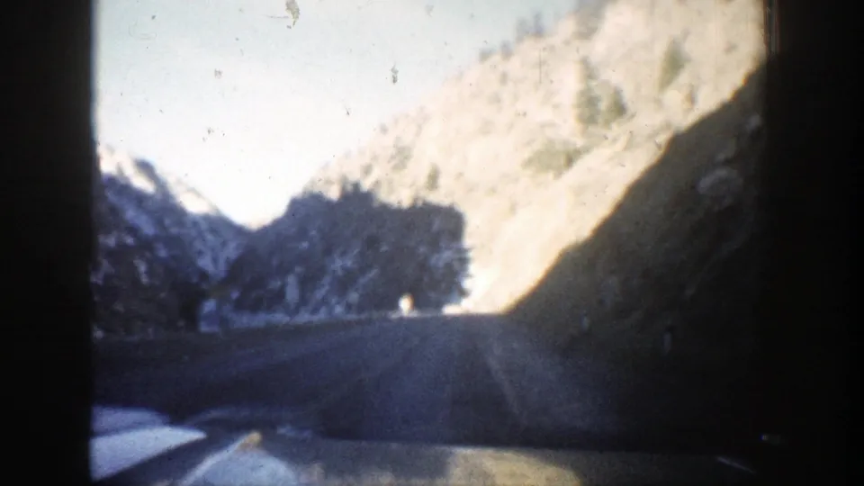 After the tunnel, the 1961 Aspen-area road opens to bright daylight, mountain slopes, and a curving highway.