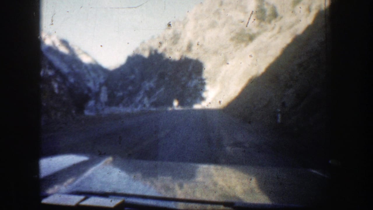 View from a moving car on a curving mountain road with snow-dusted slopes.