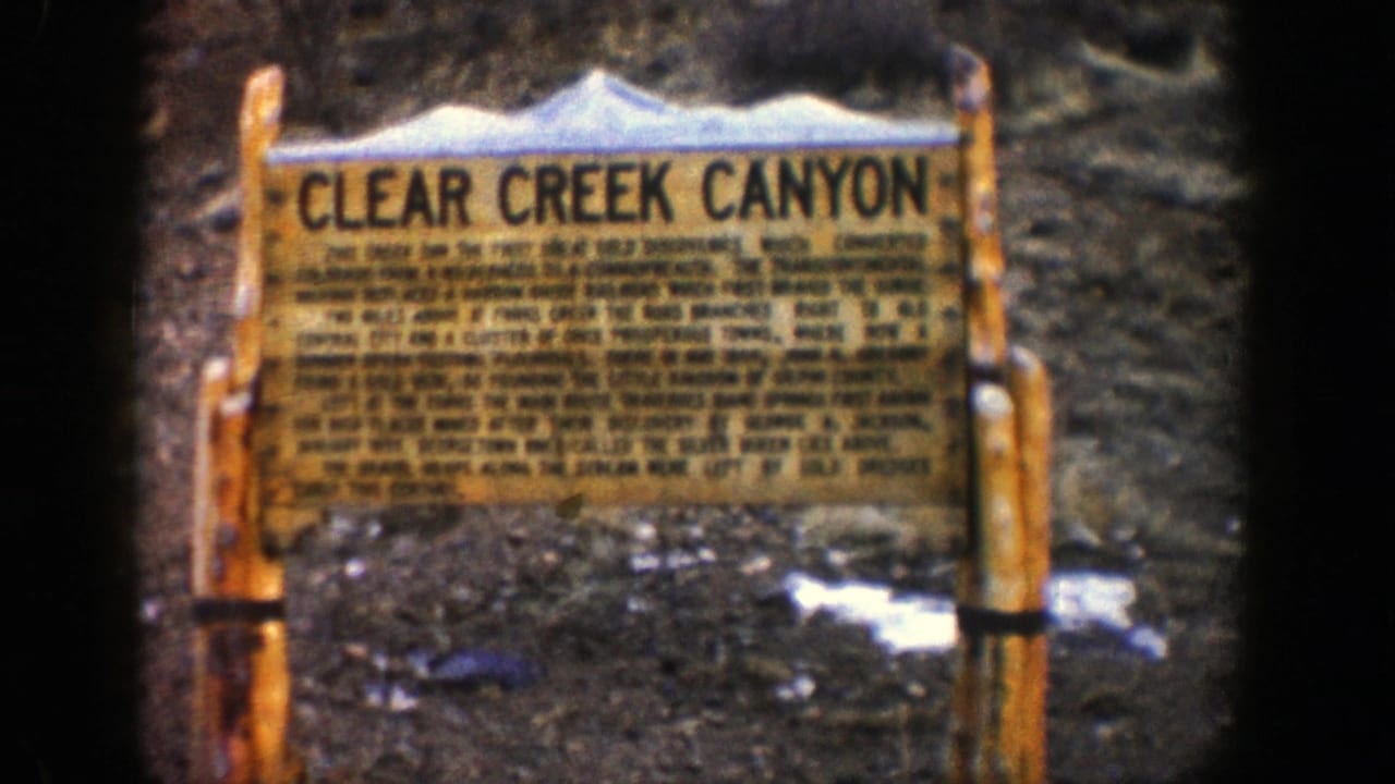 Wooden Clear Creek Canyon sign standing on rocky ground with snow patches.