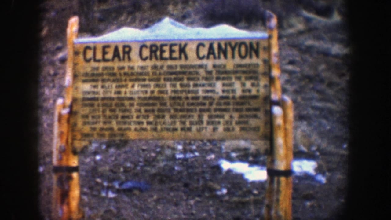 Wooden Clear Creek Canyon sign beside snow patches and rocky ground.