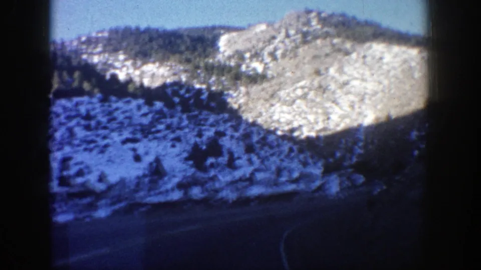 1960s 8mm frame of snow-dusted Colorado hills and a curving road seen from a moving vehicle.