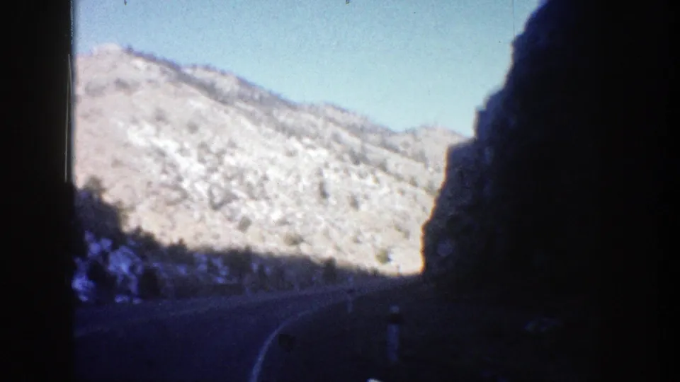 Aspen, Colorado 8mm frame showing a winding winter mountain road, bright snow on rocky slopes, and dark interior framing at right.
