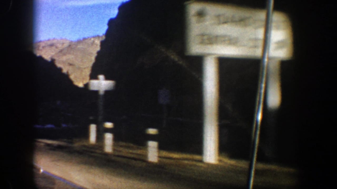 Roadside sign and white posts beside a shadowed mountain road.