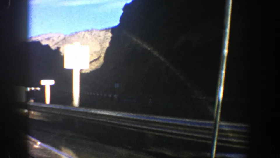 A bright sign and guardrail flash by as the home-movie camera tracks along a mountain road near Aspen in 1961.