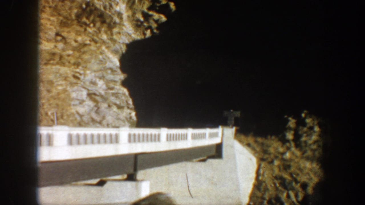 White bridge crosses a rocky canyon wall under bright sunlight and shadow.