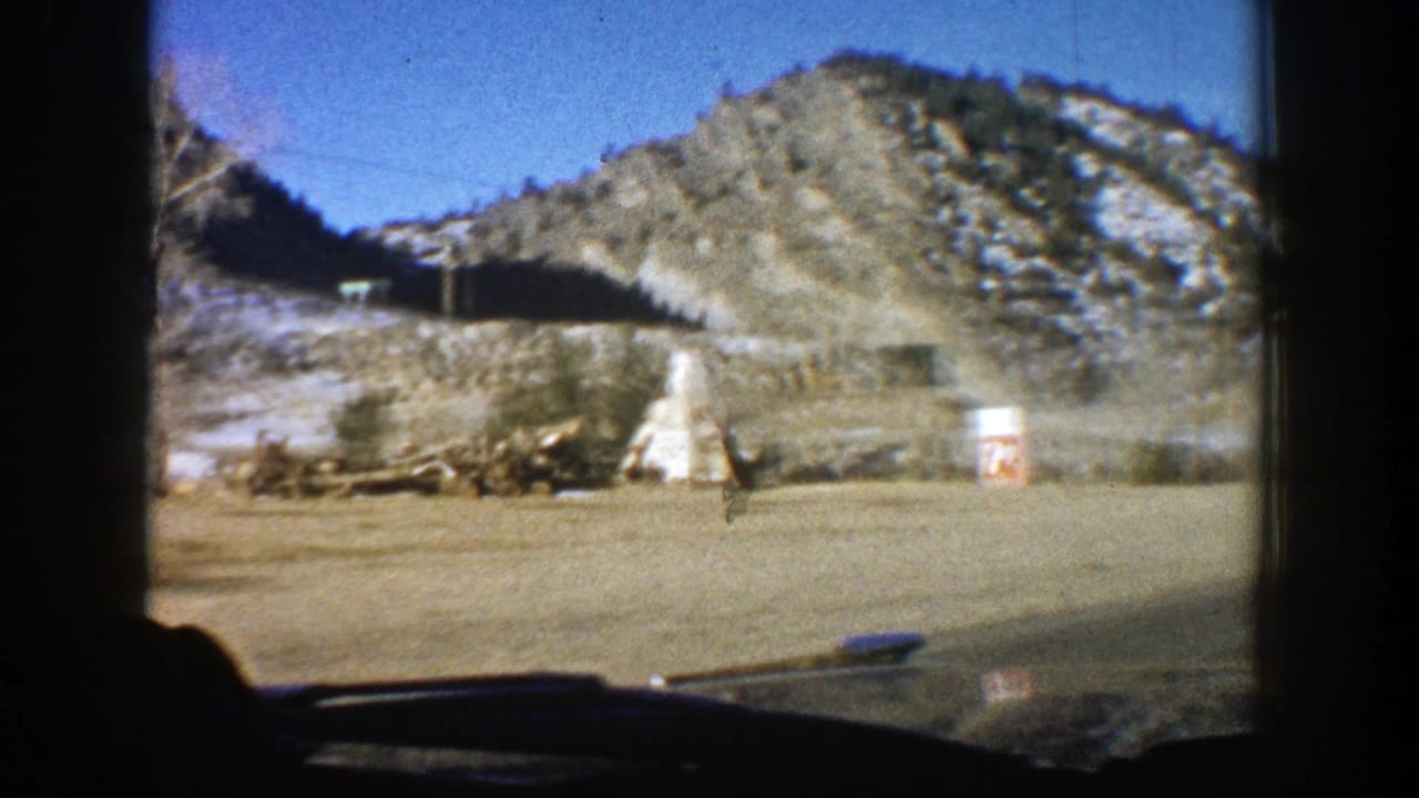 White teepee-shaped roadside structure and small sign below a rocky snowy hill.