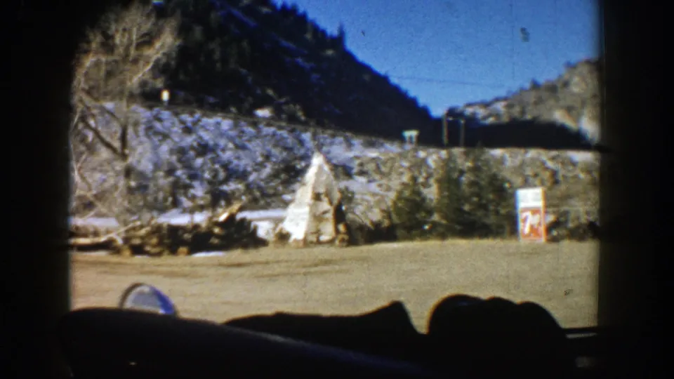 Moving 8mm road shot in Aspen showing a white teepee-shaped roadside feature, a small sign, snow patches, and a mountain slope.