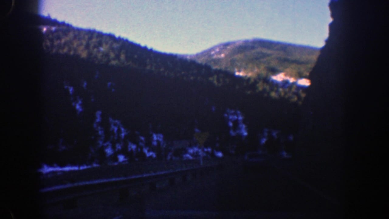 Forested mountain slopes seen through dark car-window framing under a pale blue sky.