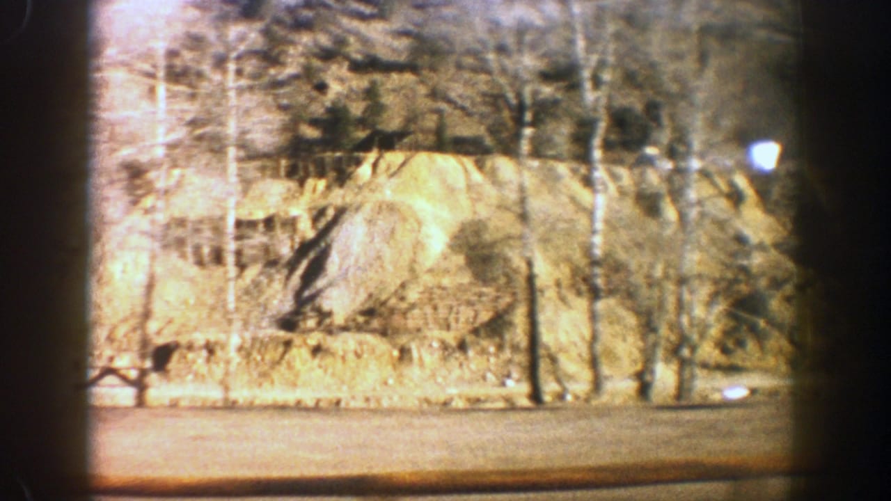 Tan rock slope beside a road with bare trees and dark film gate edges.