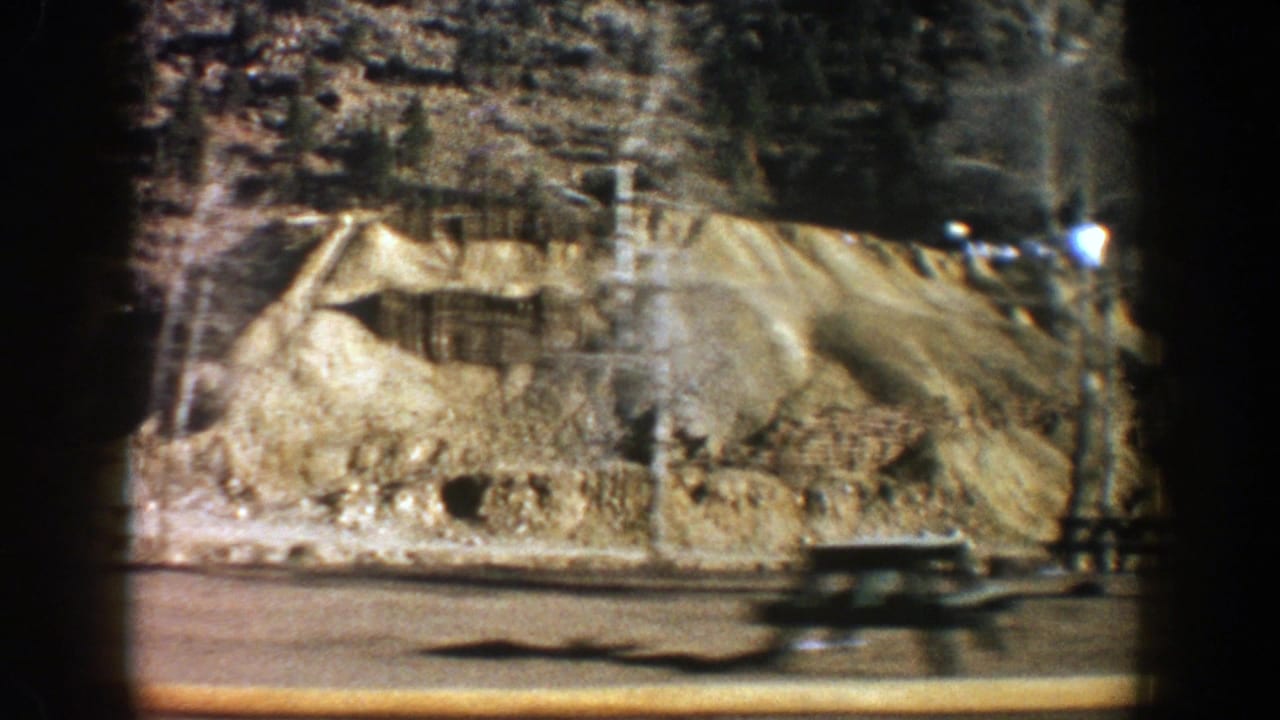 Roadside mountain base with tan rock, a bench-like object, and blurred vehicle motion.