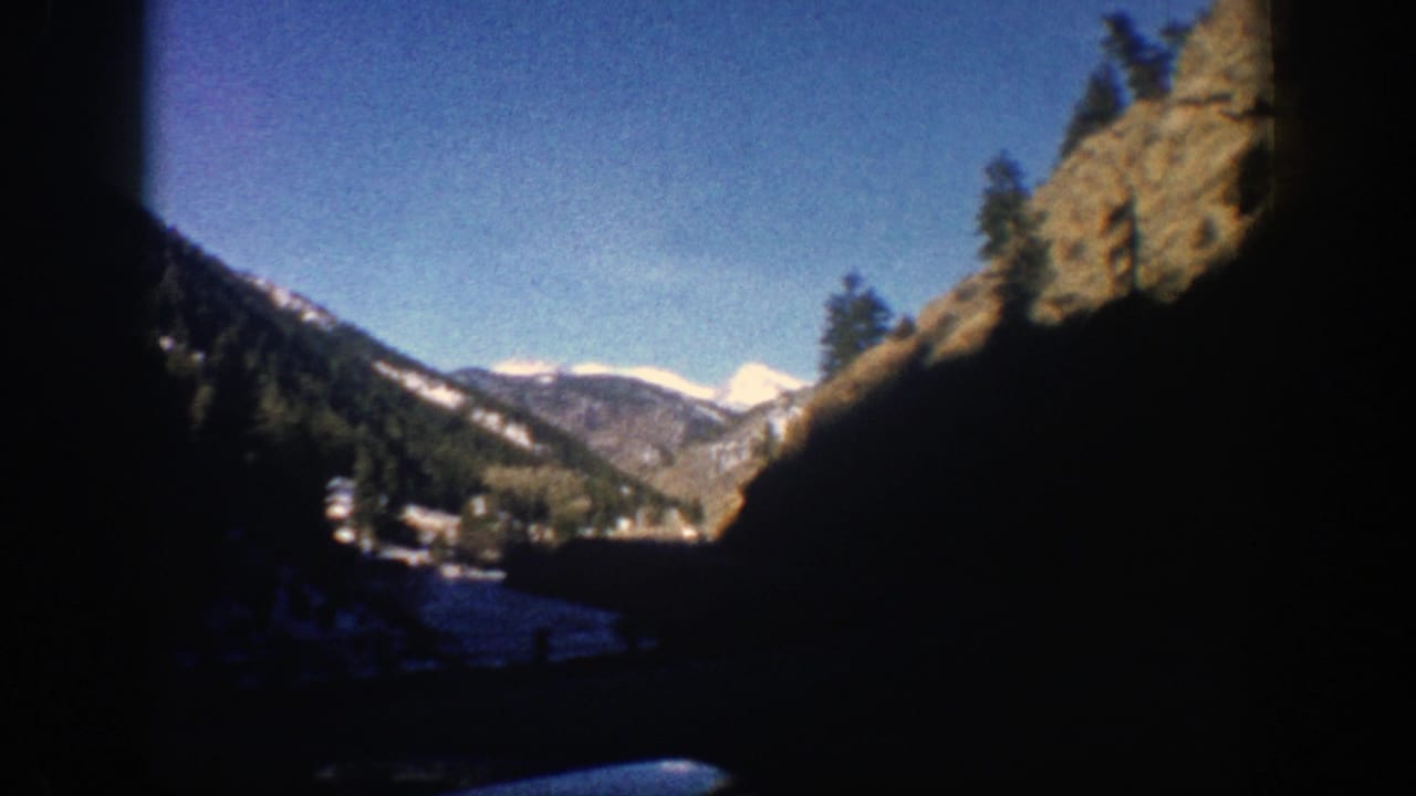 Distant snowy peaks and forested slopes framed by dark window edges during a mountain drive.