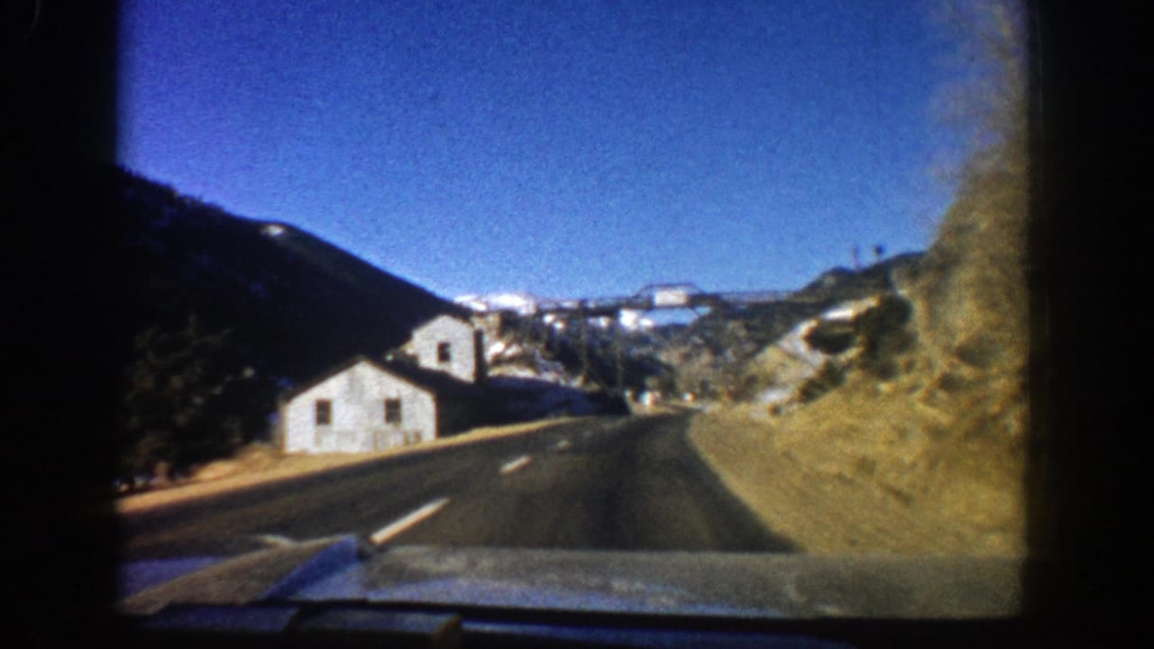 White roadside building seen closer from a curving mountain road.