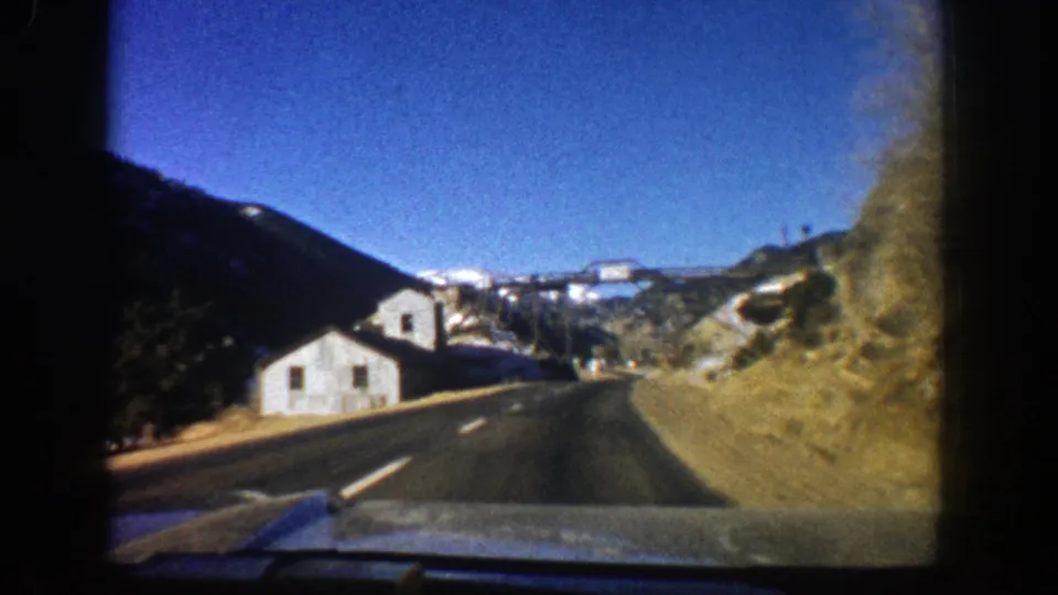 Closer 1961 Aspen-area road view of a white building below dark mountain slopes and bright sky.