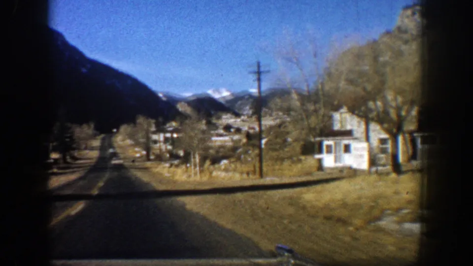 1961 Aspen roadside view from a car, showing modest houses, a utility pole, leafless trees, and mountains beyond.
