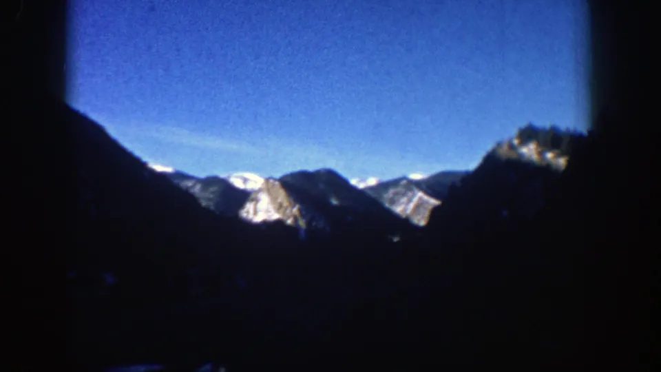 Aspen mountain view from the moving car, with dark foreground slopes and bright snow-covered peaks beneath a clear blue sky.