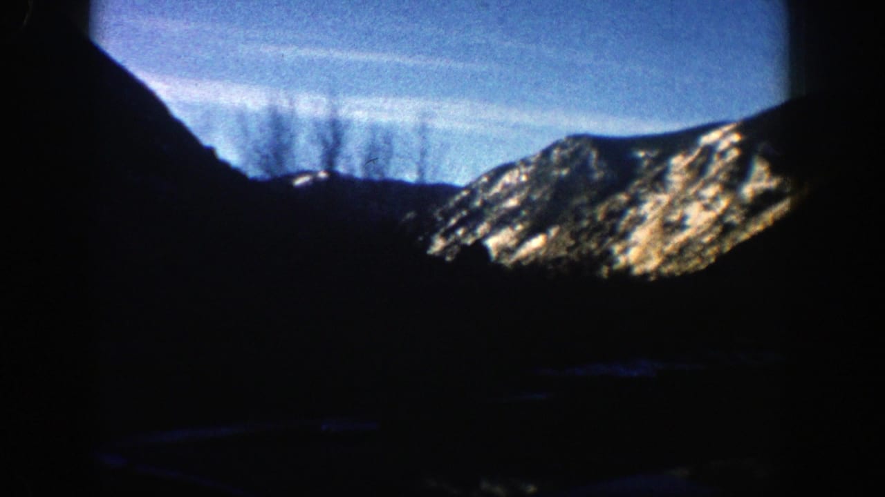Dark mountain valley with a sunlit snowy ridge in the distance.