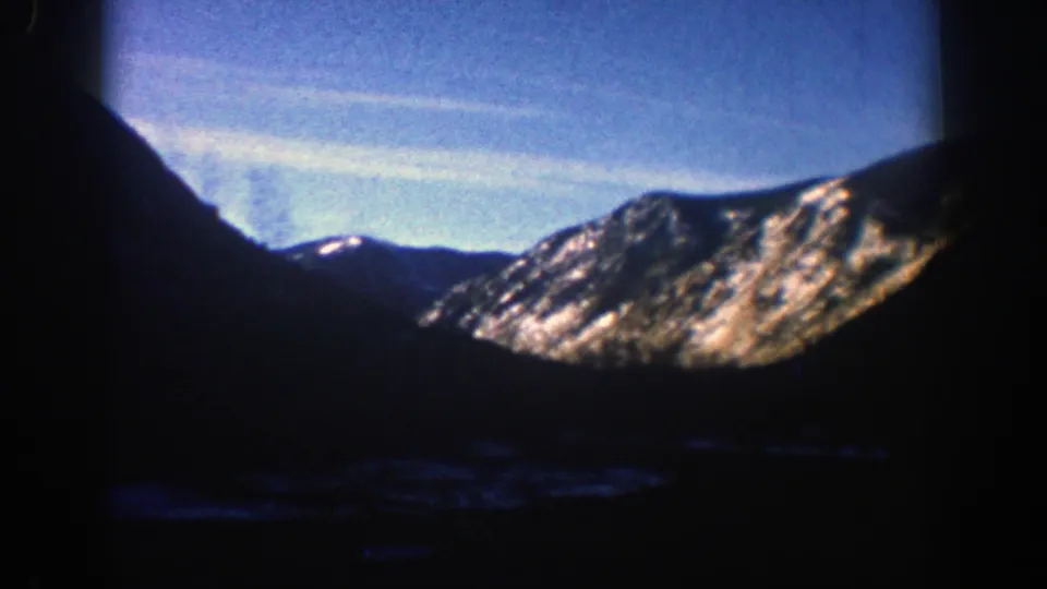 1961 Aspen-area 8mm frame showing a wide valley perspective with a dark foreground, distant snowy ridge, and pale blue sky.