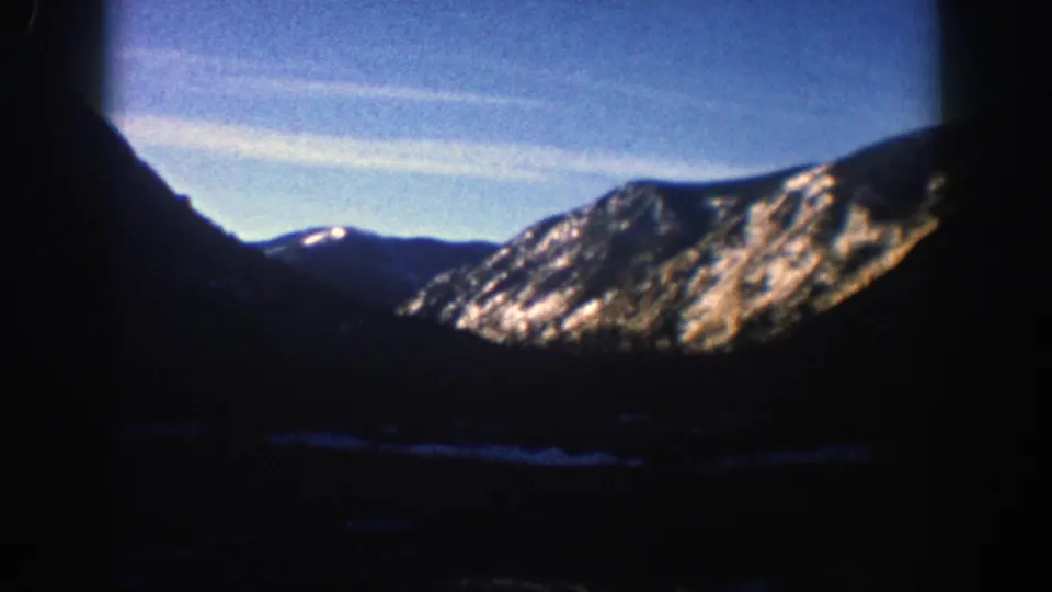1961 Aspen-area 8mm frame with a snow-dusted ridge beyond a shadowed valley, framed by dark slopes and visible film-edge vignetting.