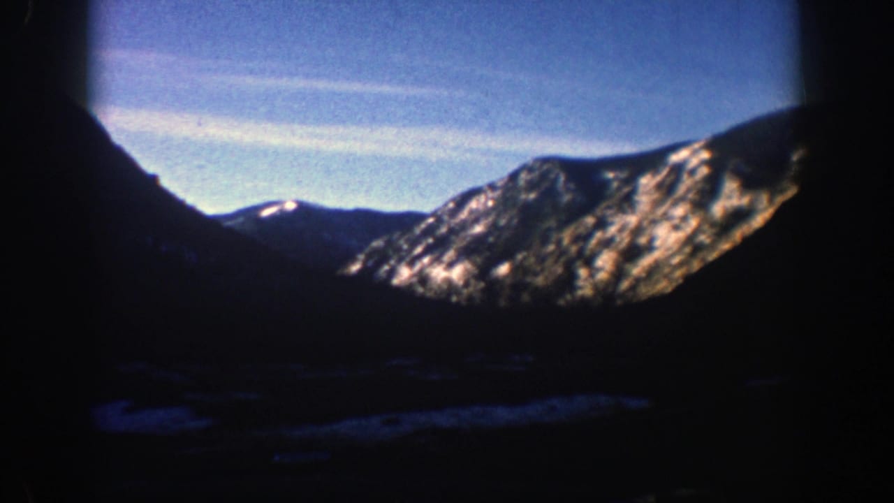 1961 Aspen-area 8mm frame showing dark mountain slopes, bright rocky ridges, snow patches, and blue sky.