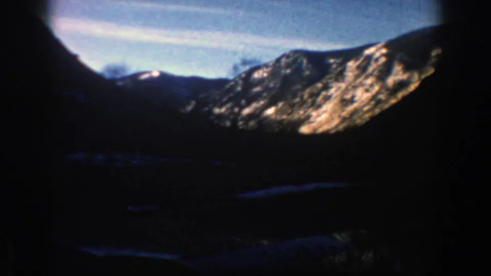 1961 Aspen-area mountain view with sunlit rock faces, shadowed valley terrain, and blue sky in an 8mm frame.
