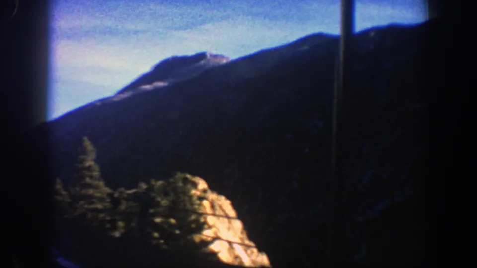 1961 Aspen-area mountain scene with evergreen trees, a sunlit rock outcrop, dark ridgeline, and soft 8mm edge shadows.