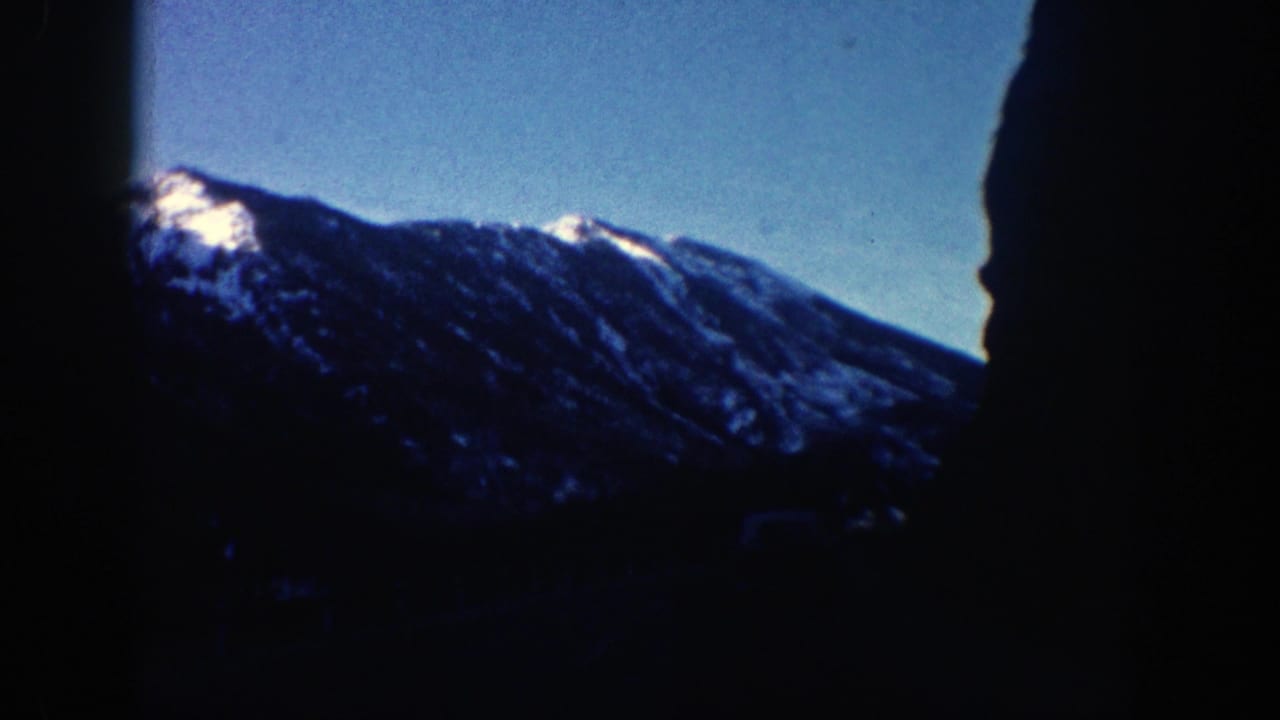 Dark mountain ridge with snow patches under a clear blue sky.