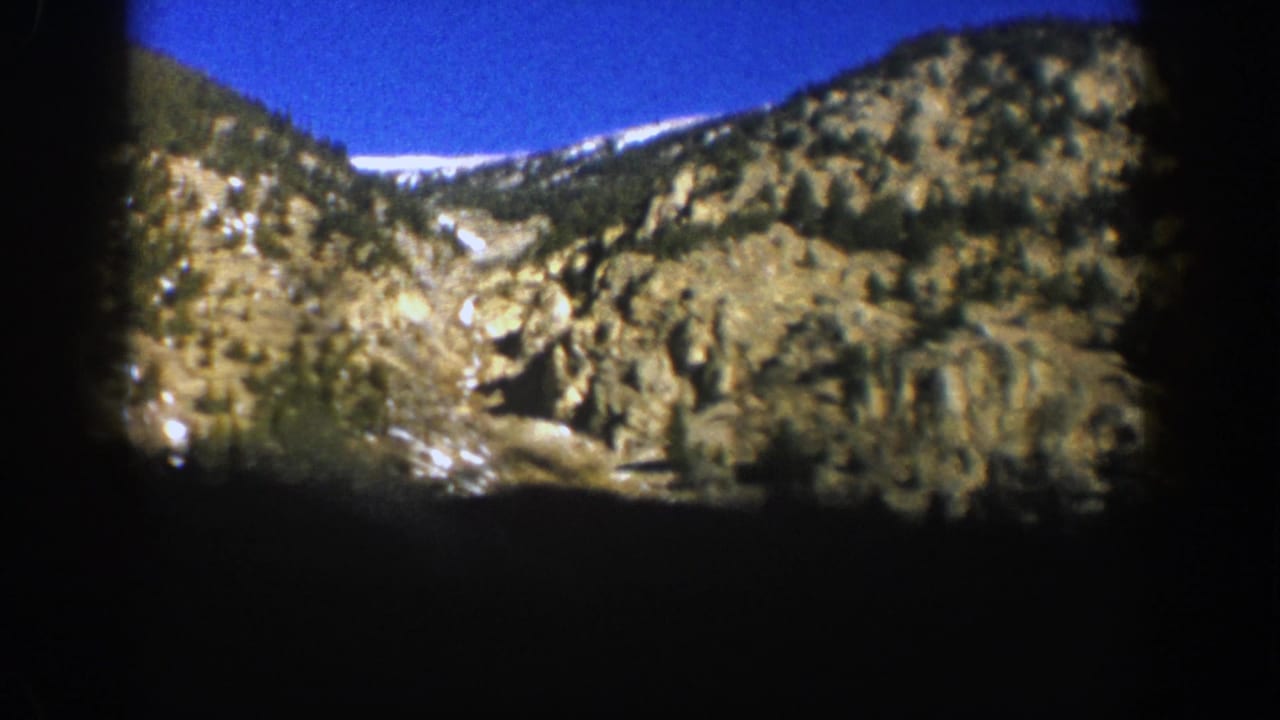 Rocky mountain slopes with snow patches under a deep blue sky and dark film borders.
