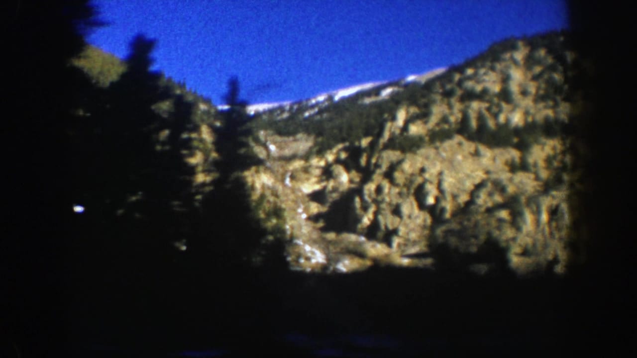 Snow-streaked rocky ridge partly obscured by dark evergreen trees.