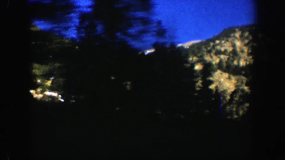 1961 Aspen, Colorado 8mm roadside view with motion blur, dark evergreens, rocky slopes, and a strong blue sky.
