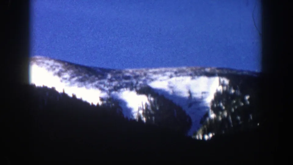1961 Aspen-area mountain view with bright snowfields, evergreen trees, and dark 8mm frame edges.