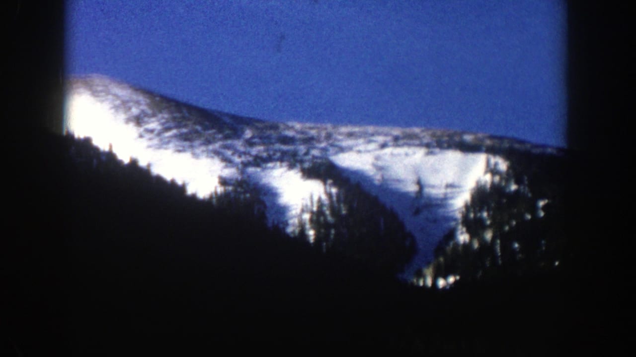 Snowy mountain ridge and dark forested slope seen through 8mm frame edges.