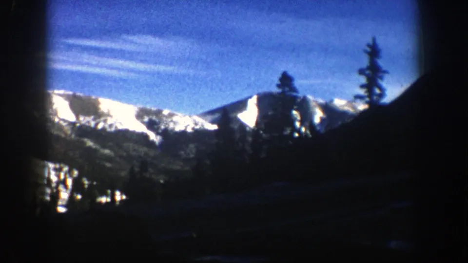 Aspen, Colorado mountain view from a moving car, with bright snow on distant peaks and silhouetted trees in the foreground.