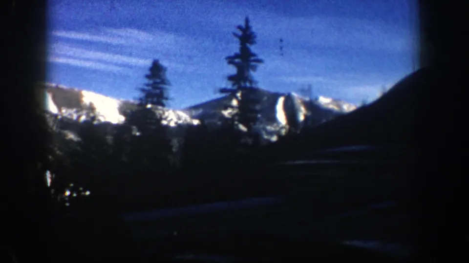 1961 Aspen mountain scenery with foreground evergreens, snow-streaked ridges, and heavy dark framing from the car interior.