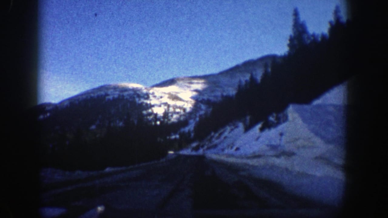 Mountain road beside snowbanks with bright snowy ridge ahead.