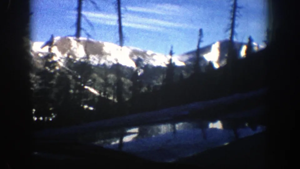 1961 Aspen-area mountain roadside view with sunlit snow, evergreen trees, utility poles and a dark foreground road edge.