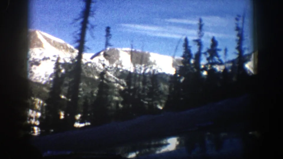 Snowy Aspen-area mountain ridge and conifers viewed from a car during a 1961 home-movie drive.