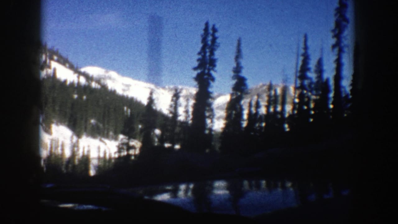 1961 Aspen, Colorado home-movie frame showing snow-capped mountains and evergreens seen from inside a car.