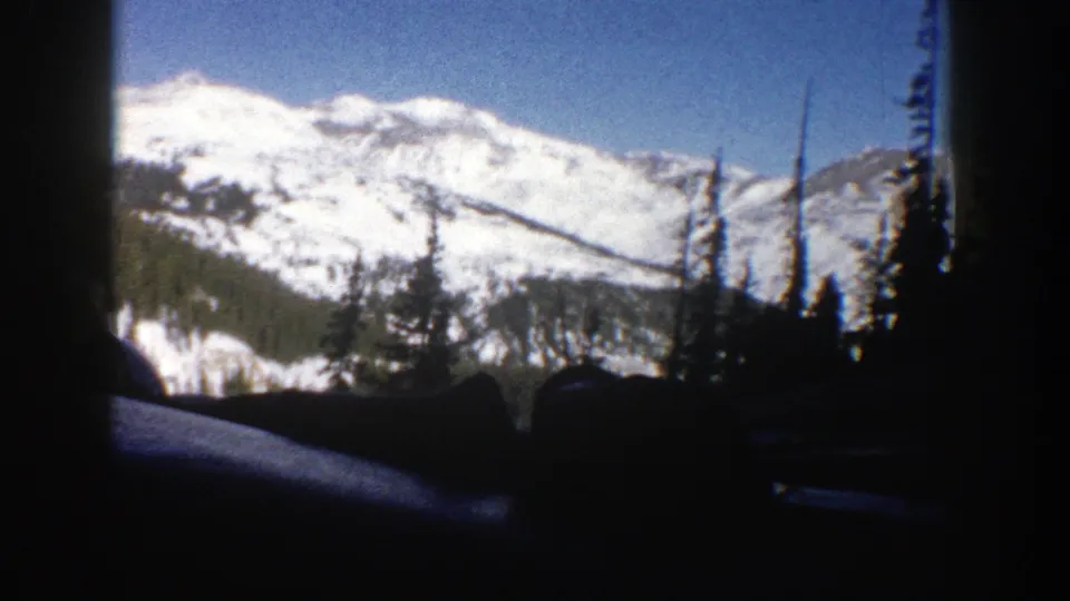 1961 Aspen, Colorado frame of a bright snowy mountain slope seen past dark car-window framing and forested lower hills.