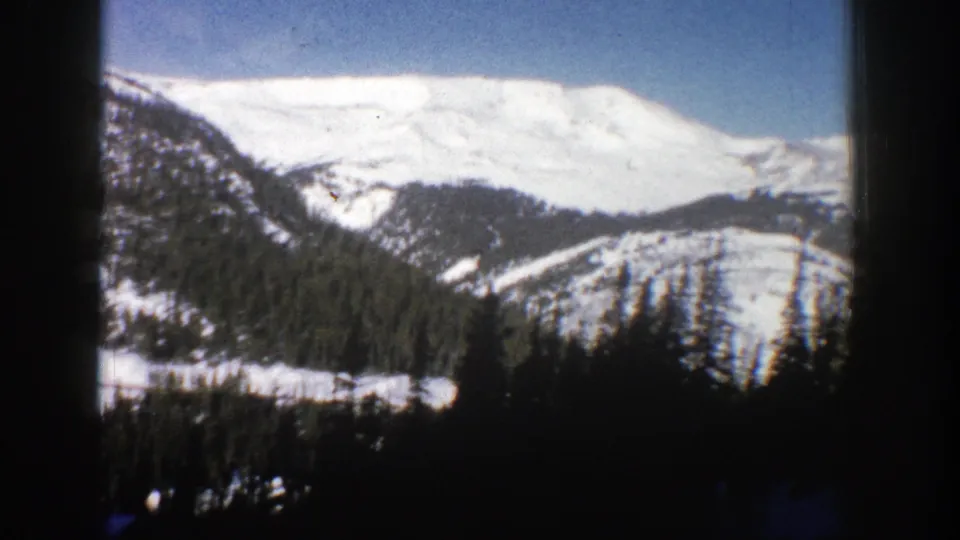 Snow-covered Aspen-area mountain face and lower forested slopes filmed in soft, high-contrast 8mm color.
