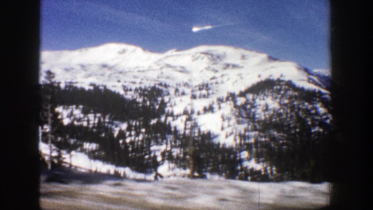 Snowy mountain ridge and tree-covered slope framed by dark film edges.