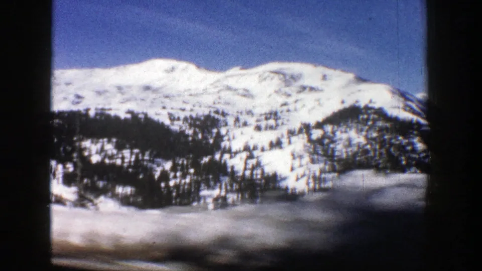 1961 Aspen, Colorado home-movie view of snowy slopes and evergreens, with motion-blurred foreground suggesting filming from a moving car.