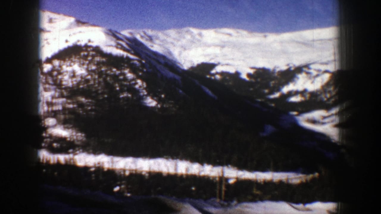 1961 Aspen, Colorado 8mm frame showing snow-covered mountain ridges, dark tree tops, and a winter valley under blue sky.