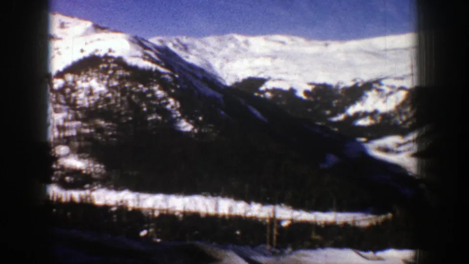 1961 Aspen, Colorado 8mm frame showing snow-covered mountain ridges, dark tree tops, and a winter valley under blue sky.