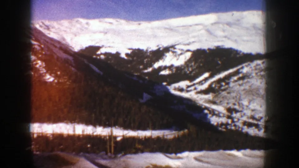 1961 Aspen, Colorado 8mm frame with snow-bright ridges, a shadowed forested slope, and warm color flare from the film scan.