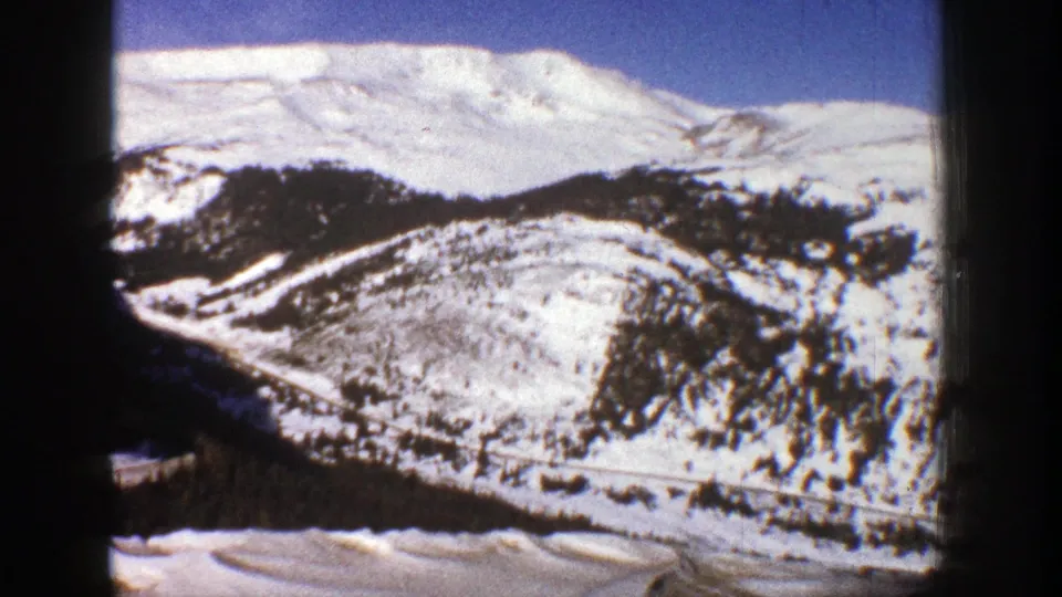 1961 Aspen, Colorado 8mm frame with a broad snow-covered hillside, scattered dark trees, and distant mountain ridge.