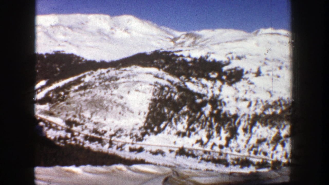 Snow-covered mountain slopes with dark trees and a road below, framed by black film edges.