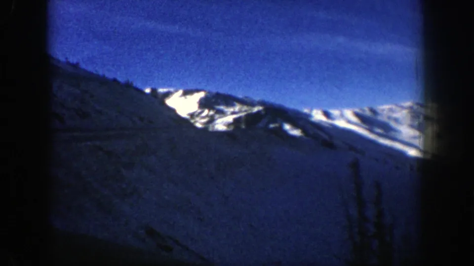 1961 Aspen, Colorado 8mm frame showing a snow-capped mountain ridge beneath a deep blue sky, seen through dark film edges.