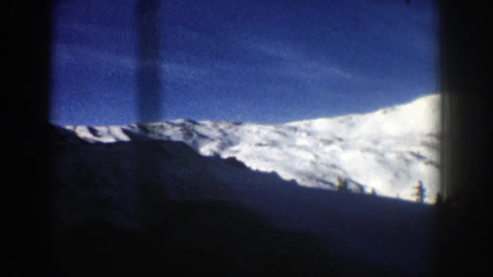 1961 Aspen, Colorado frame showing a broad snowy ridge, dark foreground terrain, faint trees, and heavy 8mm frame borders.