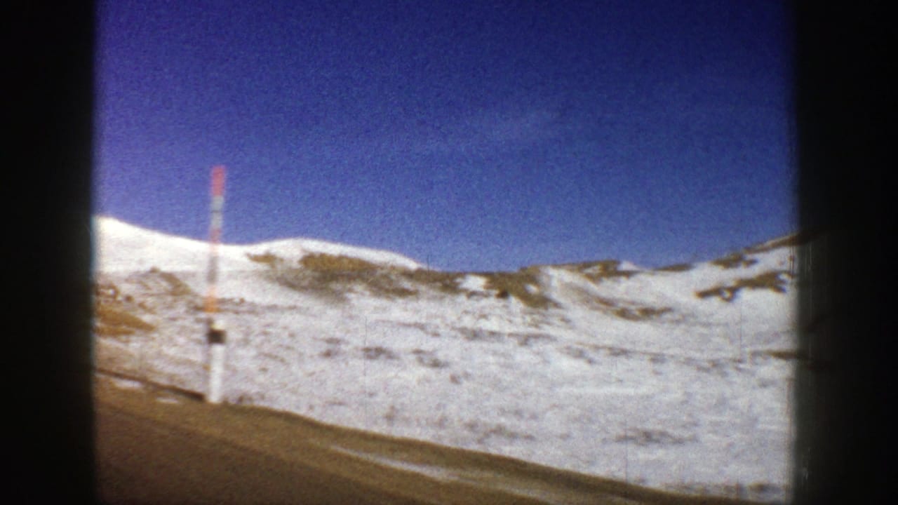 Snowy mountain slope beside a road with a red-and-white roadside marker.