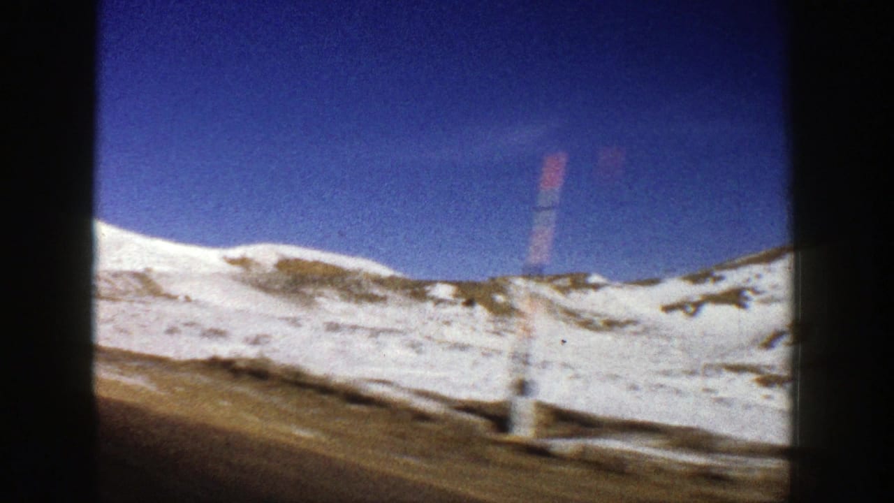 Snowy hillside and roadside marker seen through dark film-frame edges.